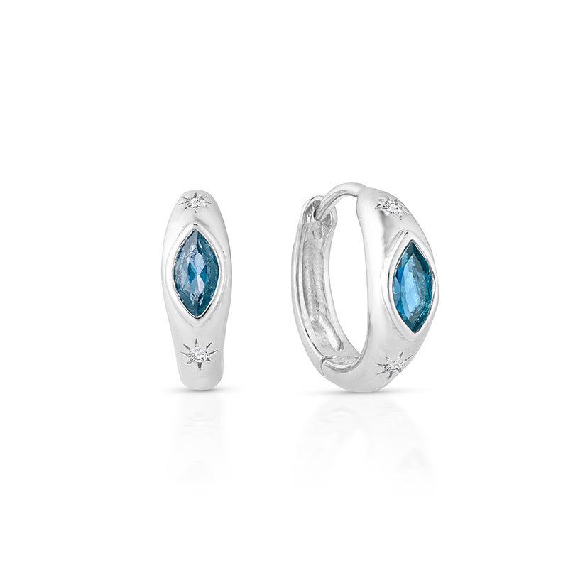 A pair of silver huggie hoop earrings with marquise-cut blue gemstones and small starburst accents, shown on a clean white background.