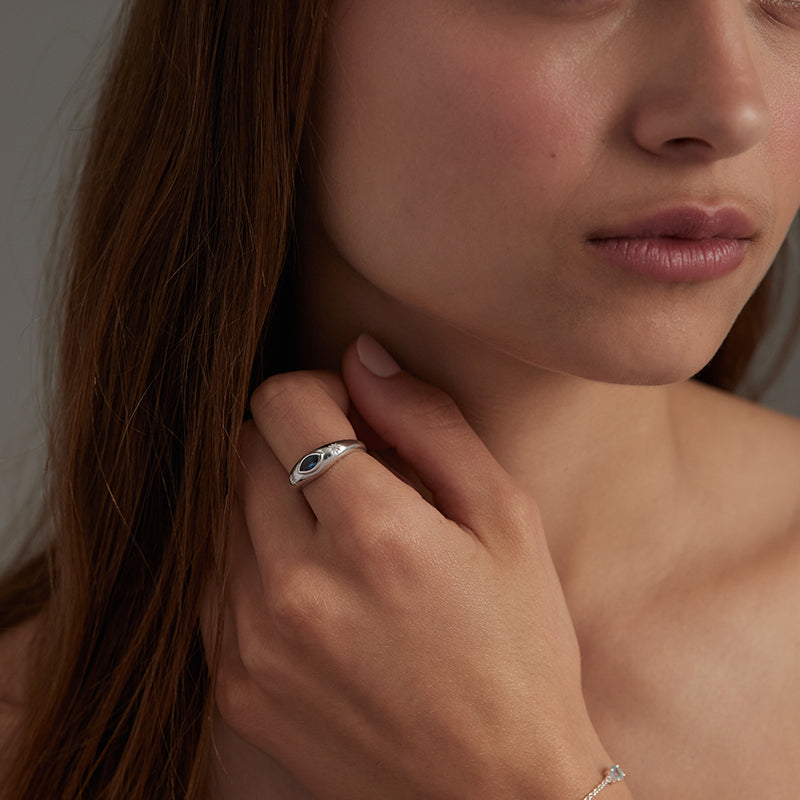 A close-up lifestyle shot of a woman wearing a silver ring with a black and white eye design on her finger, with a delicate silver bracelet visible on her wrist.