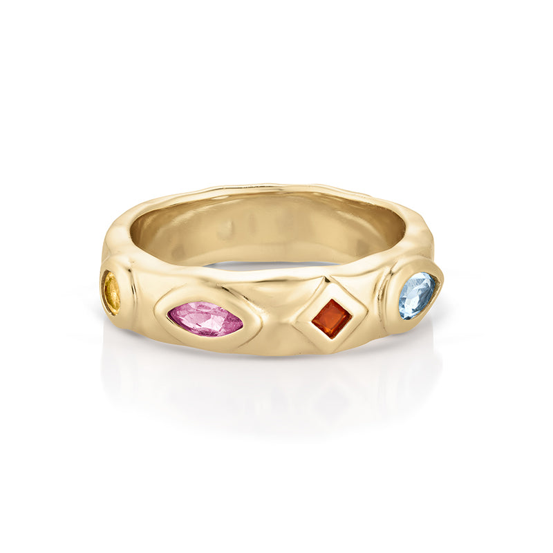 A gold band ring featuring bezel-set multicolor gemstones, including a marquise-cut pink stone, a round orange stone, a round blue stone, and a small yellow stone, shown on a white background.