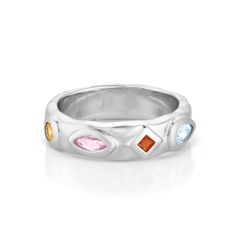 A silver band ring featuring four small, colorful gemstones in different shapes (oval, marquise, diamond, round) set into a textured, wavy silver band, shown on a white background with a soft reflection.