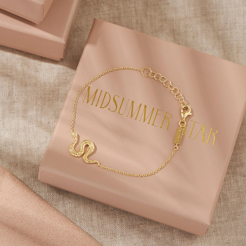 Gold bracelet on a pink 'MIDSUMMER STAR' box with a beige fabric background
