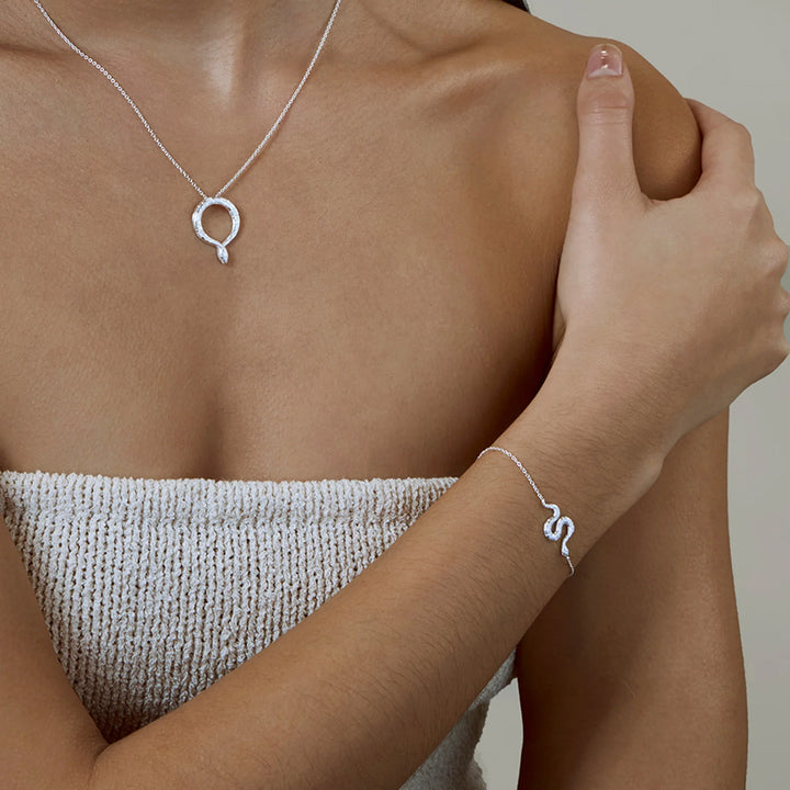 Person wearing a silver necklace and bracelet with a minimal background