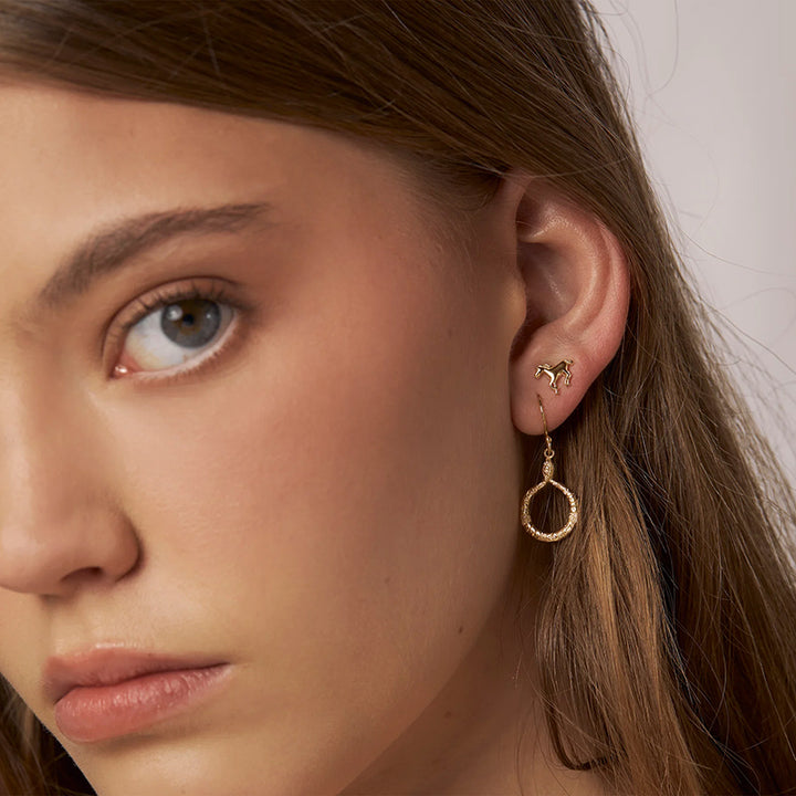 Close-up of a woman wearing gold hoop earrings with a neutral background