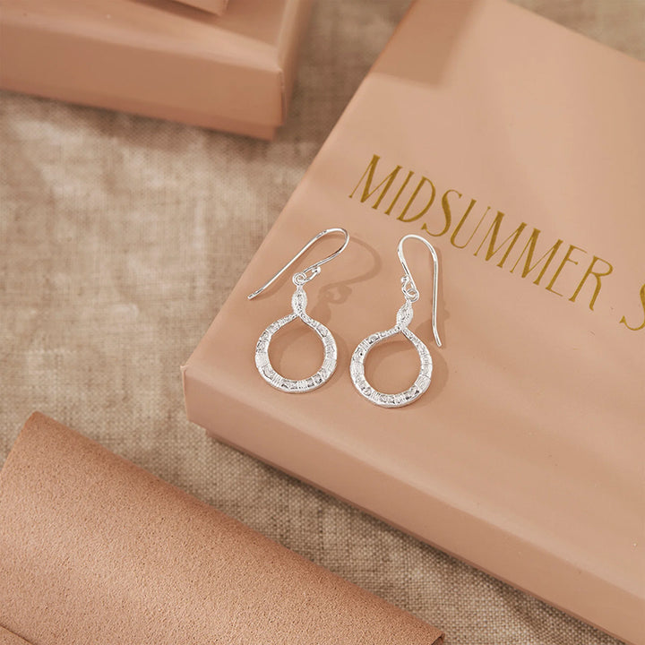 Silver earrings on a 'Midsummer' branded box with a brown fabric background
