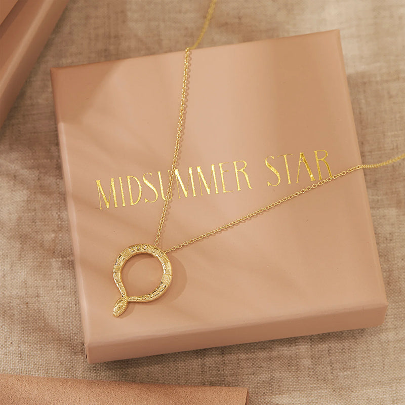 A gold necklace with a textured circular pendant resting on a beige gift box printed with the brand name 'MIDSUMMER STAR'.